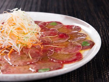 Koyu arkaplandaki hafif tabaktaki mermer sığır carpaccio, yatay fotoğrafı kapat.