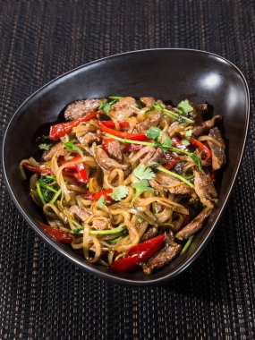 Tava, sığır dilimlenmiş kızarmış şehriye, soya soslu dolma biber ve maydanoz, koyu arka planda bir kasede servis edilmiş, dikey fotoğraf.