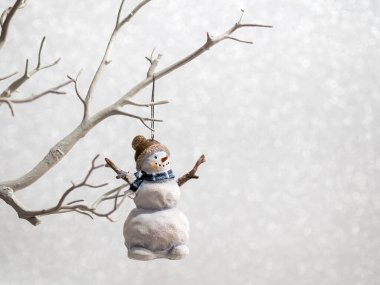 Noel süsü Kardan Adam gümüş renkli arka planda bir ağaç dalında asılı duruyor.