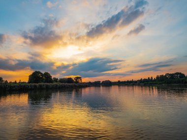 Akşamları nehir üzerinde dramatik bulutlarla gökyüzü. Bulutlar ve nehirde dramatik gün batımı. Doğa manzarası, yansıma, mavi bulutlu gökyüzü ve turuncu güneş ışığı, gün batımında manzara. 