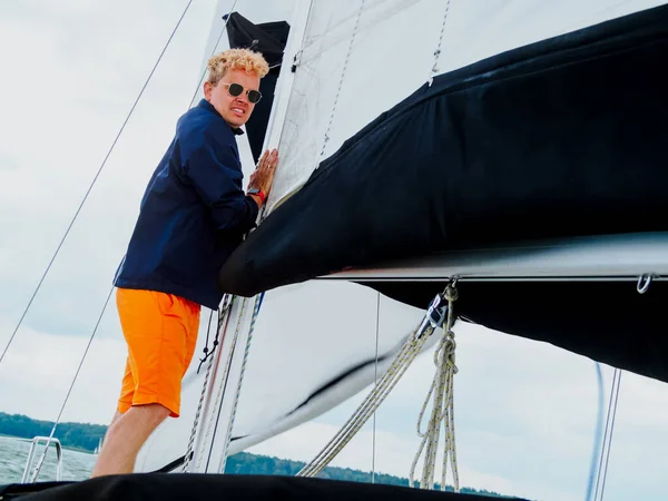 young person a crew member lowering sail on sailing yacht because rain and storm begin