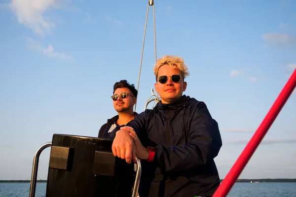 一对同性恋夫妇在帆船上 一个人驾驶着帆船 另一个人正站在船边 望着夕阳西下的景色 — 图库照片