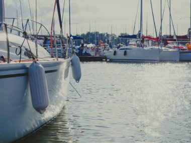 İskelede demirli yelkenli yatlar ve yatın gövdesinde ve suda güneş parlıyor.