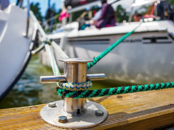 A white sailing boat moored with a line tied around a metal fixing. Mooring rope and bollard for recreational boats at the harbor. Close up photo of mooring hook at jetty