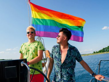 Gay çiftin lgbt gökkuşağı bayrağıyla yelkenli bir yatta tatili var.