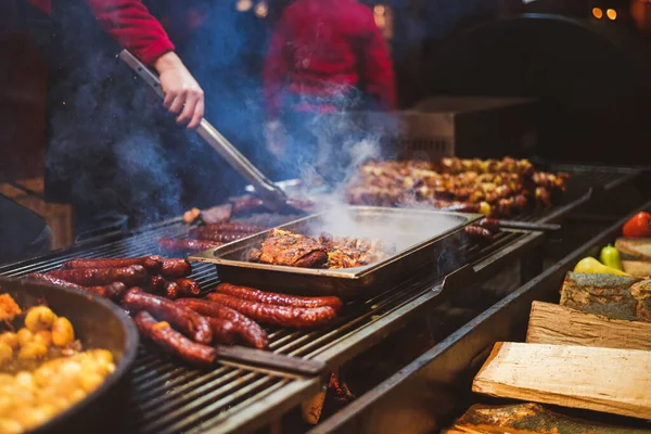 Outdoor street food festival. Chief cooking sausages, meat and potatoes cooking on an outdoor griddle