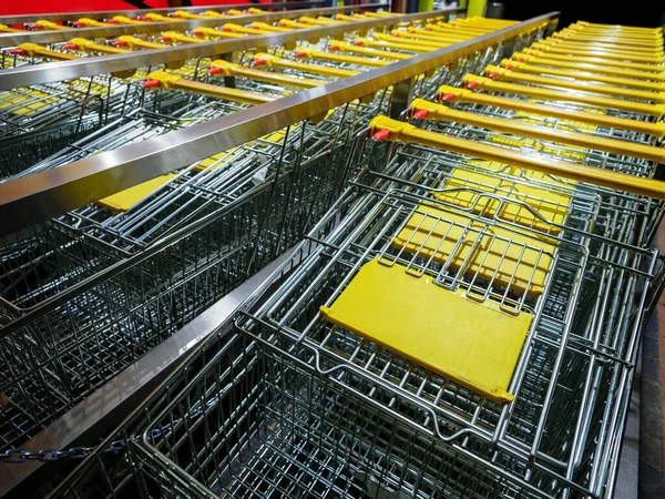 Row of stacked metal shopping trolley carts with yellow handles near of supermarket