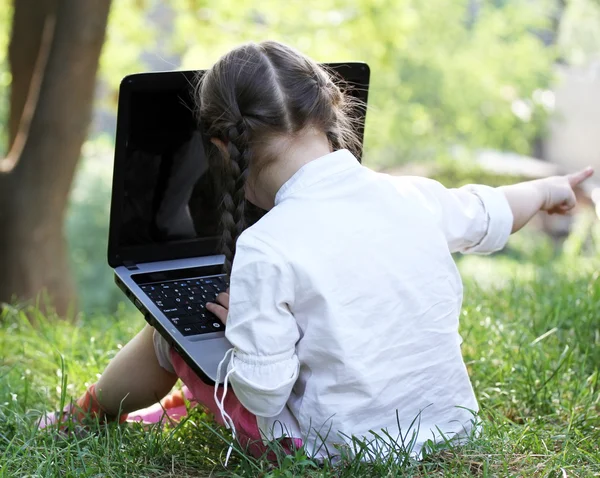 Cute little girl is sitting in the park with her laptop Stock Picture