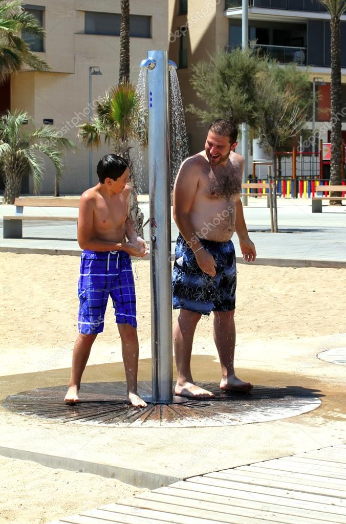 Man with 11 years old boy under the shower at beach.