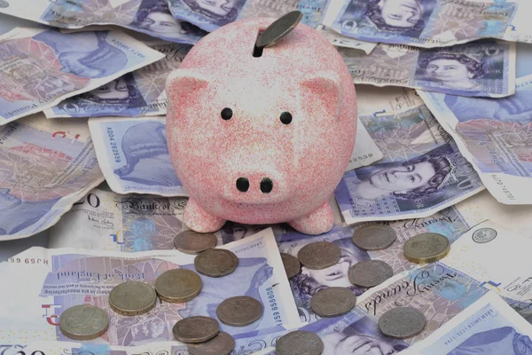 Piggy bank over notes and coins — Stock Photo, Image