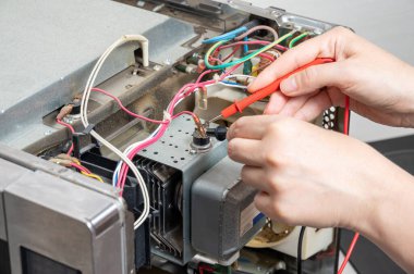 Mikrodalga fırının tamiri. Bir kadın elektriksel özelliklerini test edenle ölçer..