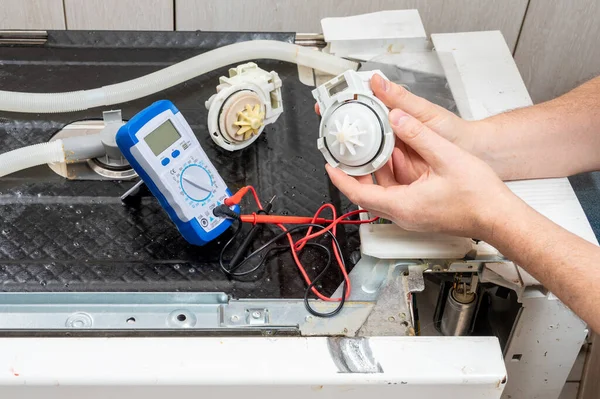 A new pump for dishwasher in the hands of a men, against the background of a disassembled dishwasher