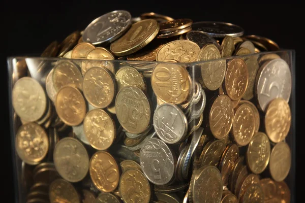 Monedas en un frasco de vidrio sobre un fondo negro — Foto de Stock