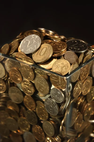 Monedas en un frasco de vidrio sobre un fondo negro — Foto de Stock