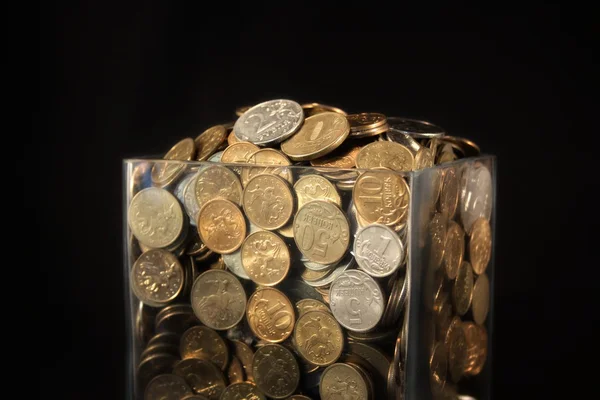 Monedas en un frasco de vidrio sobre un fondo negro — Foto de Stock