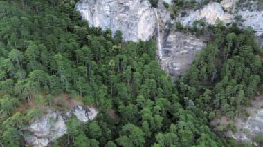 Dağların tepesindeki kayalık yeşil ormanlardaki bir şelalenin hava görüntüleri.