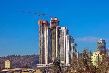 Construction of new high-rise buildings in Coquitlam City, industrial construction site, construction equipment, several construction cranes on the background of blue sky