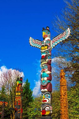Three totem poles in Stanley Park, Vancouver surrounded by green trees and against a blue cloudy sky
