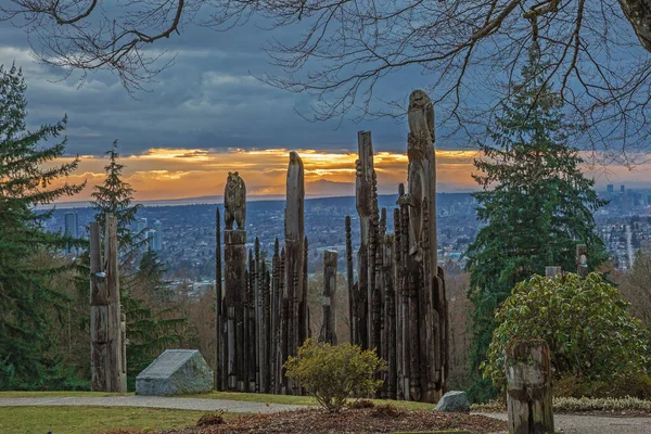 Native American Indian First Nations totem poles in Burnaby Mountain Park Totem poles and tall trees against an evening cityscape and stormy cloudy sky