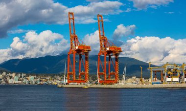 Vancouver limanındaki okyanus gemilerini yüklemek için mavi bulutlu bir gökyüzü ve dağ sırasının arka planına karşı. Kuzey Vancouver, dağ sırasının eteklerinde.
