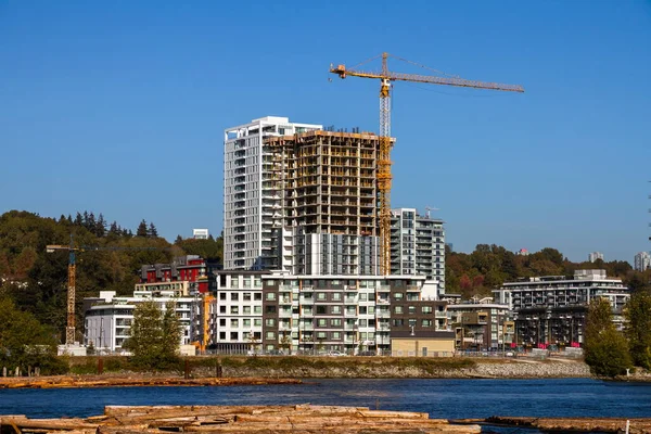 Construction of a new residential district at the riverbank in  Vancouver City. The river bank of Fraser River and the slope covered with forest on the background of a blue sky