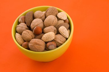 Badem ve fındık bir kase içinde, turuncu arka plan ile.