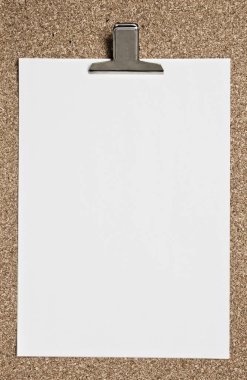 Blank paper with metal clip on cork surface.