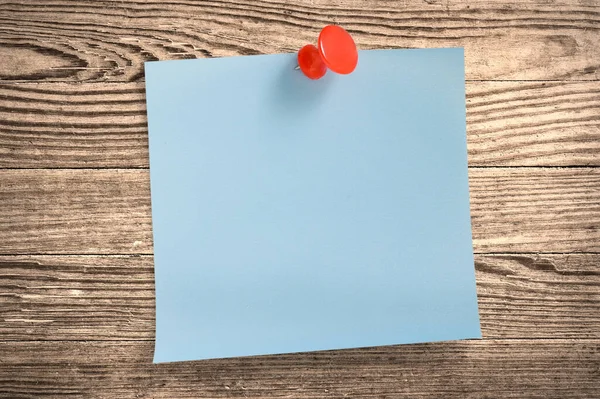 Blue paper note with thumbtack on wooden surface, clipping path.