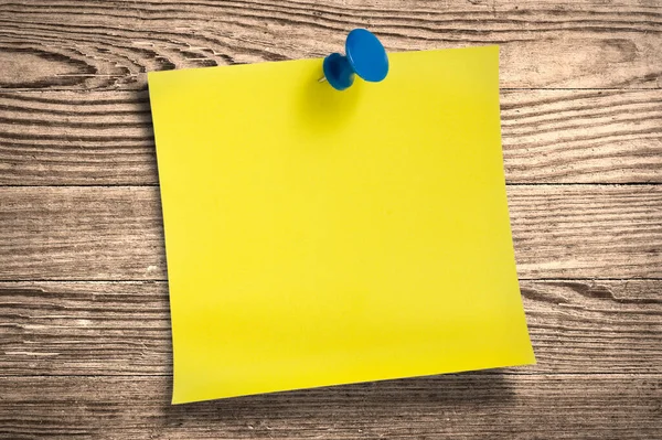 Yellow paper note with thumbtack on wooden surface, clipping path.