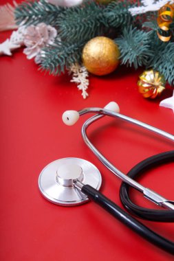 Kırmızı arka planda tıbbi steteskop ve Noel süslerini kapatın. Noel medikal konsepti dikey biçimi