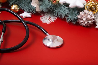 Kırmızı arka planda tıbbi steteskop ve Noel süslemeleri. Noel medikal konsepti