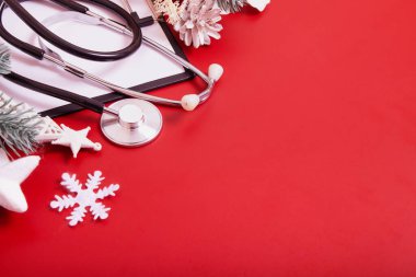 Tıbbi steteskop ve fotokopi alanı olan kırmızı arka planda noel süslemeleri olan bir pano. Tıbbi Noel konsepti