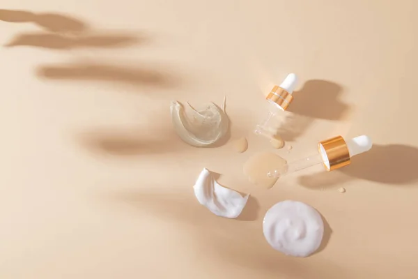 Bej bir arka planda bitkilerin gölgesiyle çeşitli kozmetik ürünlerinin ve pipetlerin kokuları