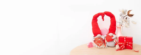 Two gnomes in love in red caps with a hearts on a white background with copy space. Valentine's day still life