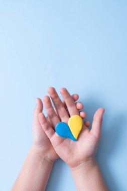 Ukrayna 'nın ulusal bayrağının sarı-mavi renklerinin kalbi çocuk ellerinde. Dikey fotoğraf.