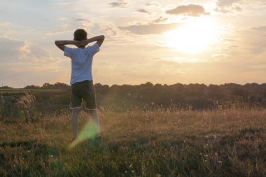 Çocuk ellerini başının arkasında kaldırdı ve sihirli günbatımının keyfini çıkardı..