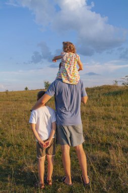 Baba ve çocuklar dışarıda omuzlarında. Köy kavramının doğasında aile var..