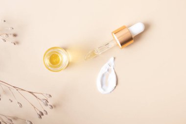 Pipetli kozmetik şişesi ve bej arka planda krem lekesi..