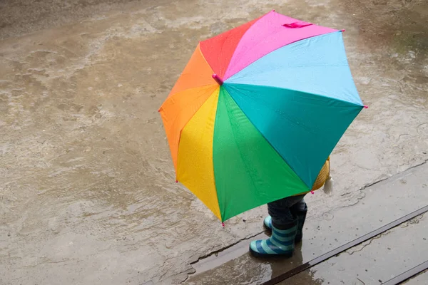 Трехлетняя девочка прячется под дождем под цветным зонтиком — стоковое фото