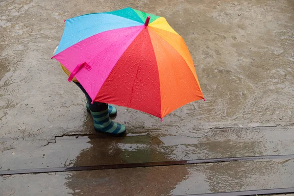 Трехлетняя девочка прячется под дождем под цветным зонтиком — стоковое фото