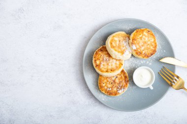 Ekşi kremalı ve pudra şekerli bir tabakta kızarmış peynirli kek..