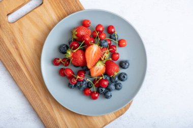 Çilekler, kirazlar ve yaban mersinleri koyu bir tabakta, üst manzara.