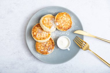 Ekşi kremalı ve pudra şekerli bir tabakta kızarmış peynirli kek..