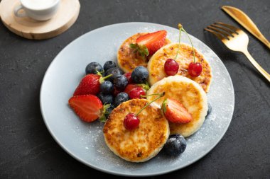 Pudra şekerli ve böğürtlenli bir tabakta kavrulmuş peynirli kek..