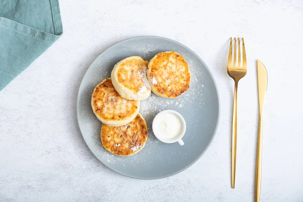 Ekşi kremalı ve pudra şekerli bir tabakta kızarmış peynirli kek..