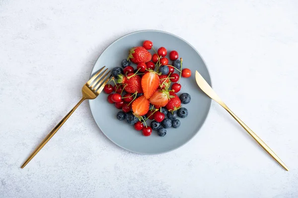 Bıçak ve çatalla bir tabakta çilek, kiraz ve yaban mersini..