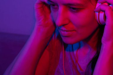 Kulaklıklı güzel genç bir kadın neon ışıkta müzik dinlemekten hoşlanıyor..