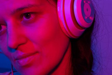 Kulaklıklı güzel genç bir kadın neon ışıkta müzik dinlemekten hoşlanıyor..