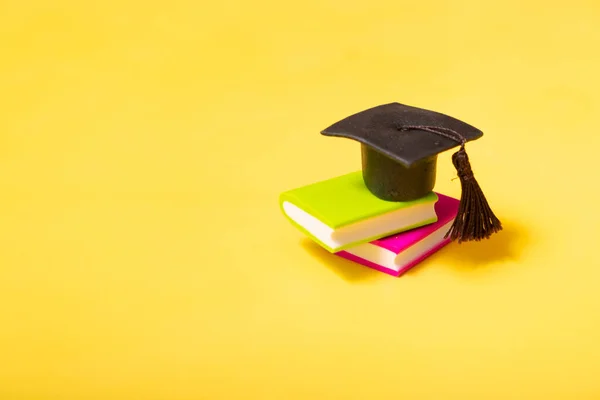 Graduation cap on colorful books on yellow background. Education concept with copy space.