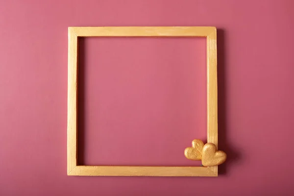 Square golden frame blank with golden hearts on red background. Flat lay, top view, copy space.